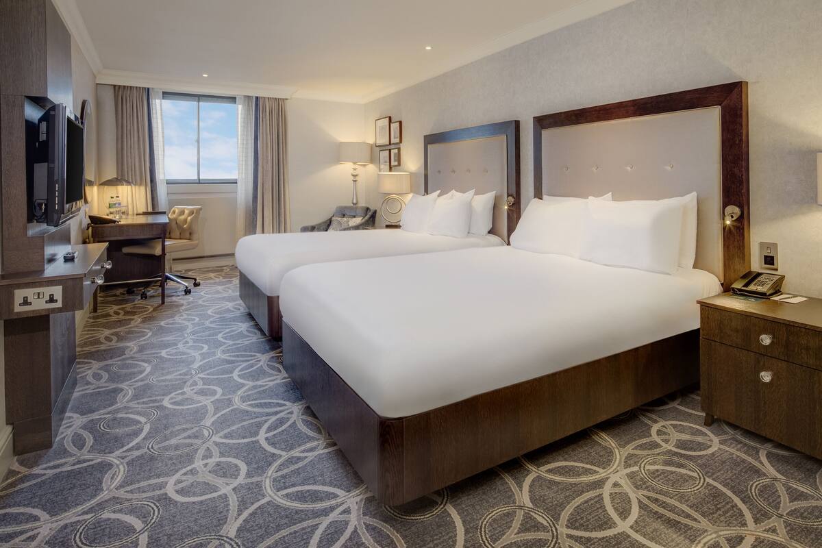 Ein Hotelzimmer mit zwei Betten, einem Schreibtisch, einem Stuhl, einem Fernseher und einem Telefon.