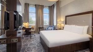A hotel room with a large bed, a desk with a chair, a TV, and a window with curtains.