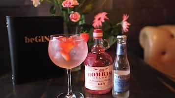 Una copa de cóctel con una decoración de fresa, una botella de ginebra Mombasi Club Strawberry & Elderflower y una botella de limonada EverTree Premium sobre una mesa.