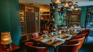 A restaurant with a long wooden table set for dining, red upholstered chairs, and a decorative column.