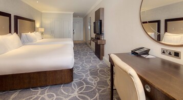 A hotel room with two beds, a desk, a chair, a TV, and a mirror.