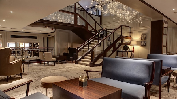 A spacious lobby with a grand staircase, comfortable seating, and a chandelier.
