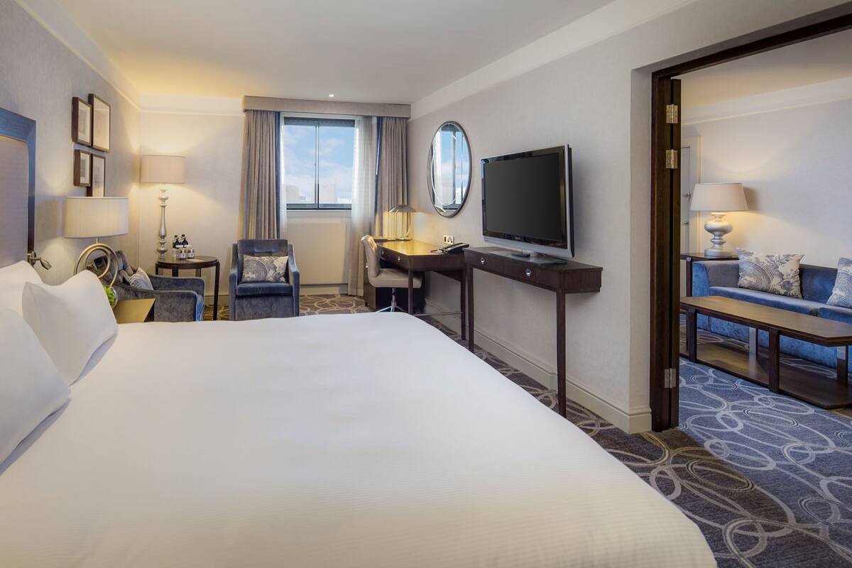 Ein Hotelzimmer mit einem großen Bett, einem Schreibtisch mit Fernseher, einer Couch und einem Sessel.