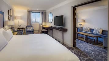 A hotel room with a large bed, a desk with a TV, a sofa, and a chair.