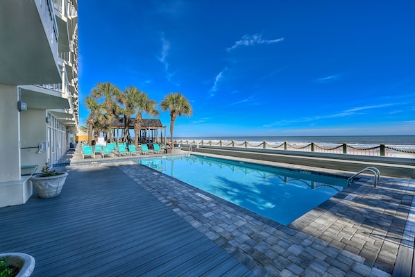 Relax by the serene pool surrounded by palm trees and lounge chairs.