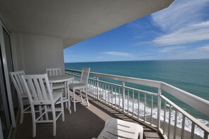 Enjoy the ocean view from this balcony with a table and chairs.