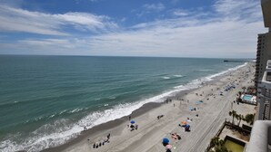 A beach with a clear sky, a long stretch of sand, and a few umbrellas. - 1001 Waters Edge Resort 3 Bedroom Condo by RedAwning (Murrells Inlet)