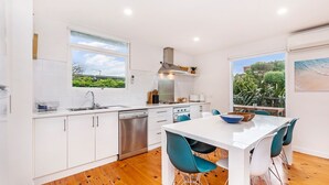 A modern kitchen with white cabinets, stainless steel appliances, and a large window offering a view of greenery. - Marlin Beach House - South Beach (Port Fairy)