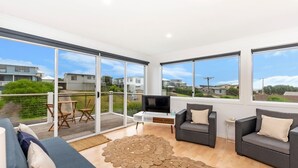 A modern living room with a TV, two sofas, a coffee table, and a large glass door leading to a balcony. - Marlin Beach House - South Beach (Port Fairy)