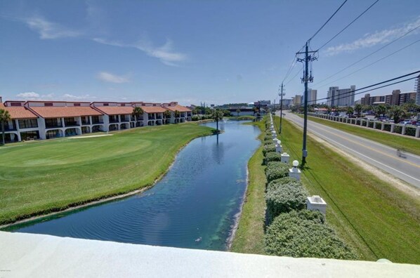 Un río atraviesa un área verde y bien cuidada, con una hilera de edificios a un lado y una carretera al otro.