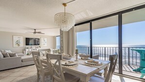 A spacious living room with a dining area, large windows, and a balcony with a view of the ocean. - Edgewater 2 Br Deluxe Gulf Front, Tower 2. Sleeps 10! (Panama City Beach)