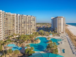 Un complexe hôtelier comprenant plusieurs immeubles de grande hauteur, un vaste espace piscine central agrémenté de palmiers et offrant une vue sur la plage.