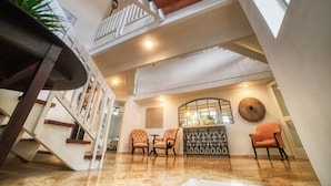 Un intérieur spacieux avec un plafond haut, un escalier et un coin salon comprenant deux fauteuils et une table.