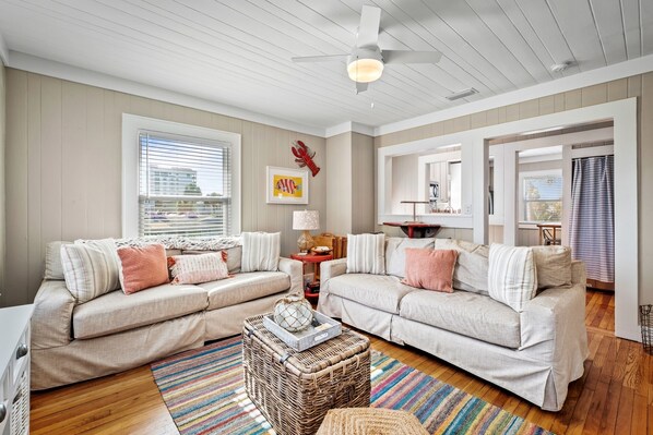 A cozy living room with two beige sofas, a wicker coffee table, and a colorful striped rug.