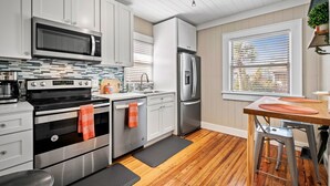 A modern kitchen with white cabinets, stainless steel appliances, and a wooden floor. - Upper-Level Duplex with Partial Ocean Views 3BR/2BA (Jacksonville Beach)