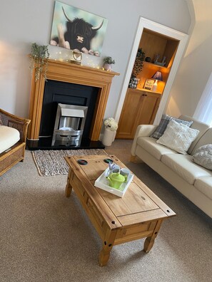 Un salon chaleureux avec une cheminée, une table basse en bois sur laquelle est posé un plateau, un canapé et un fauteuil en osier.