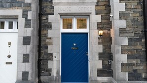 A police office with a blue door, stone walls, and a white garage door. - Old Police Office in Hawkshead by LetMeStay (Ambleside)