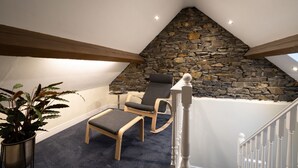 A cozy room with a stone wall, a wooden ceiling beam, a small table, a chair, and a potted plant. - Old Police Office in Hawkshead by LetMeStay (Ambleside)