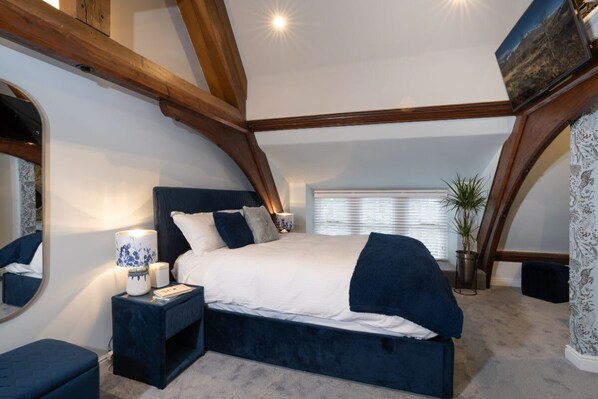 A bedroom with a large bed, a bedside table, a mirror, and a window with blinds.