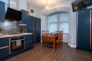A modern kitchen with dark blue cabinetry, a built-in oven, and a dining area with a wooden table and chairs.