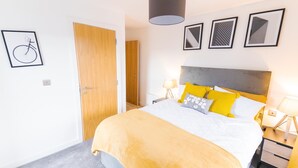 A modern bedroom with a bed, bedside tables, and a door. - 2 Bed Apartment Sleeps 4 With Free Parking (Salford)