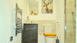 A bathroom with a dark wood cabinet, a toilet with a yellow towel, and a glass shower enclosure. - 2 Bed Apartment Sleeps 4 With Free Parking (Salford)