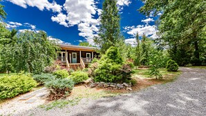 A rustic cabin with a porch, surrounded by dense greenery and a gravel driveway. - Tatum's Mtn View Retreat- SAUNA-Hiking- Unit A (Madison)
