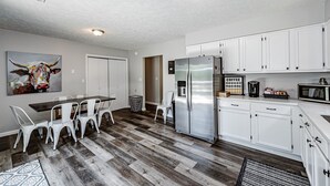 A modern kitchen with white cabinets, stainless steel appliances, and a dining area with white chairs. - Tatum's Mtn View Retreat- SAUNA-Hiking- Unit A (Madison)