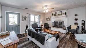 A living room with a fireplace, a ceiling fan, and a door with curtains. - Tatum's Mtn View Retreat- SAUNA-Hiking- Unit A (Madison)