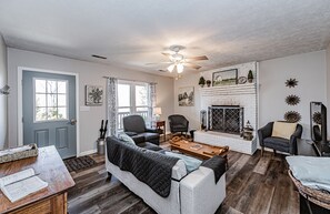 Cozy living room with a fireplace, comfortable seating area, and a ceiling fan.