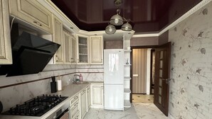 A kitchen with a gas stove, white cabinets, a refrigerator, and a patterned wall. -  PaulMarie Apartment on Podgorodskaya (Brest)