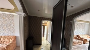 A hotel room with a large bed, a small seating area, a wardrobe, and a hallway leading to another room. -  PaulMarie Apartment on Podgorodskaya (Brest)