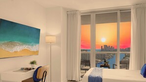 Ein Hotelzimmer mit Bett, Schreibtisch, Sessel, einem Fenster mit Vorhängen, einem Gemälde und Blick auf die Stadt.