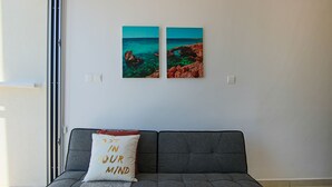 A grey sofa with a cushion that reads "LOST IN YOUR MIND" and two framed pictures of a coastal landscape on the wall behind it. - Phaedrus Living: Seaside Luxury Flat Harbour 102 (Paphos)