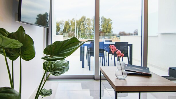 A modern office space with a large window, a desk with a vase of pink flowers, and a plant. - Phaedrus Living: Seaside Luxury Flat Harbour 102 (Paphos)