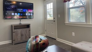 Ein Wohnzimmer mit flachbildfernseher an der Wand, einer Holzkassette, einer farbenfrohen Glasskulptur und einem Fenster mit einem gestreiften Vorhang.