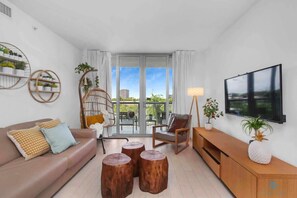 A modern living room with a sofa, wooden coffee table, a TV, and a balcony with a view. - Tropical Apartment w/Balcony|Pool|Up To 4+ Gym (Hallandale Beach)