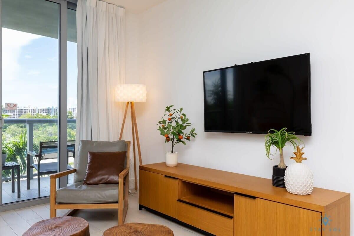 A modern living room with a sofa, a TV, a floor lamp, and a potted plant.