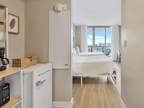 A hotel room with a bed, a coffee machine, a refrigerator, and a view of the city. - 2BR w/ Balcony + Amazing Pool + Gym (Hallandale Beach)