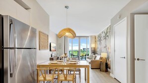 Una cocina moderna con un refrigerador de acero inoxidable, una mesa de comedor con sillas, una lámpara colgante y vistas al exterior a través de amplios ventanales.