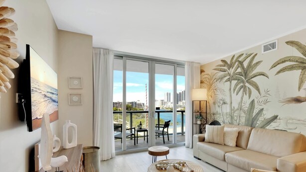 Una sala de estar moderna con un sofá, televisor y un balcón con vistas a la ciudad.