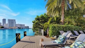 A poolside area with lounge chairs, a view of the city skyline, and a palm tree. - Spectacular Apartment w/Balcony+ Pool+ Near Beach (Hallandale Beach)
