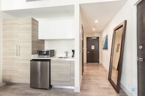 Kitchen features a refrigerator, microwave, and sink, with light wood cabinetry and a white countertop.