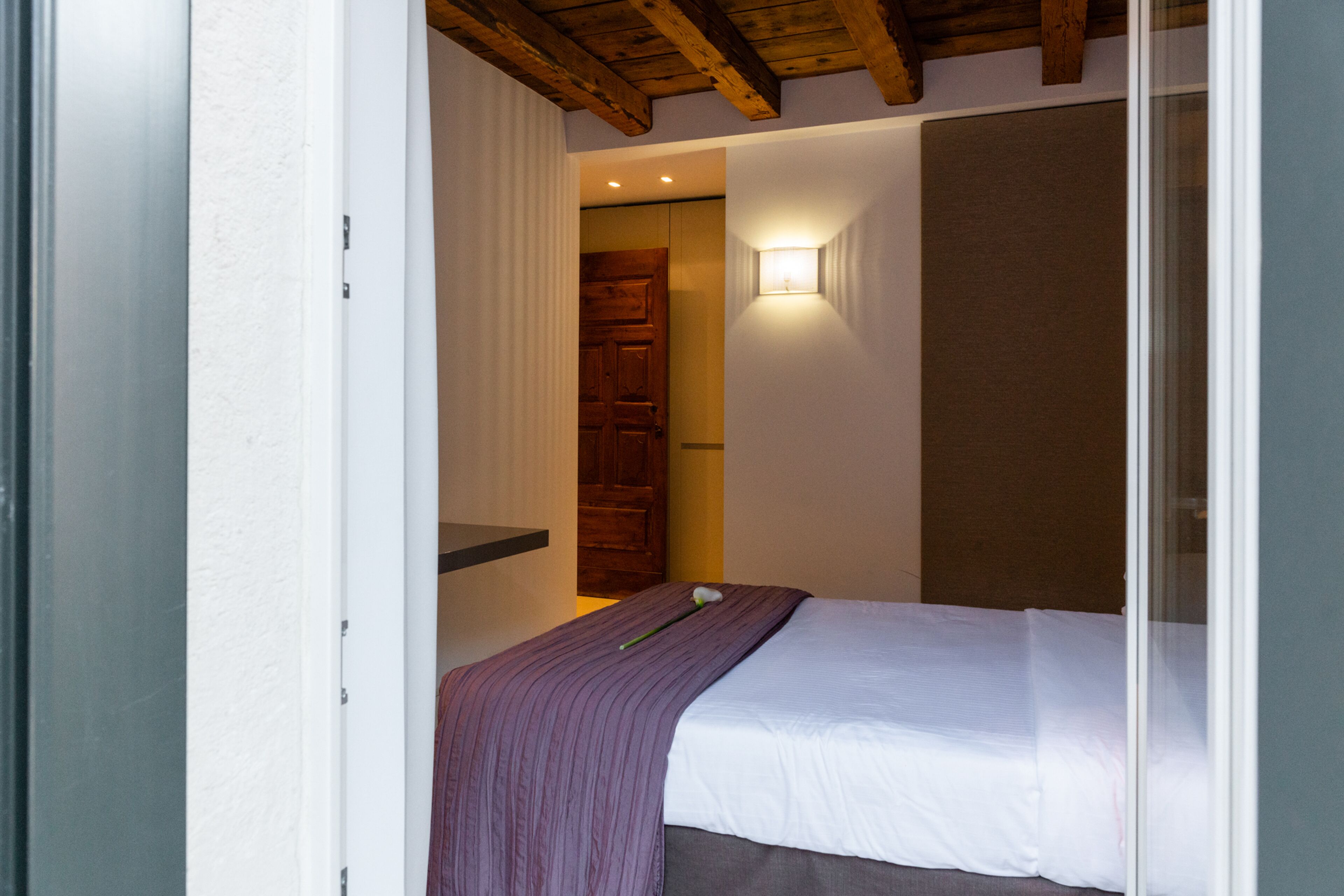 A bedroom with a bed, a wooden door, and a wall-mounted light.