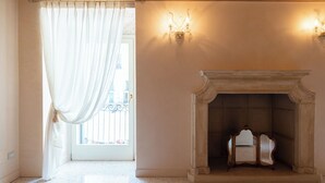 A room with a fireplace, a large window with curtains, and a wall-mounted light fixture.