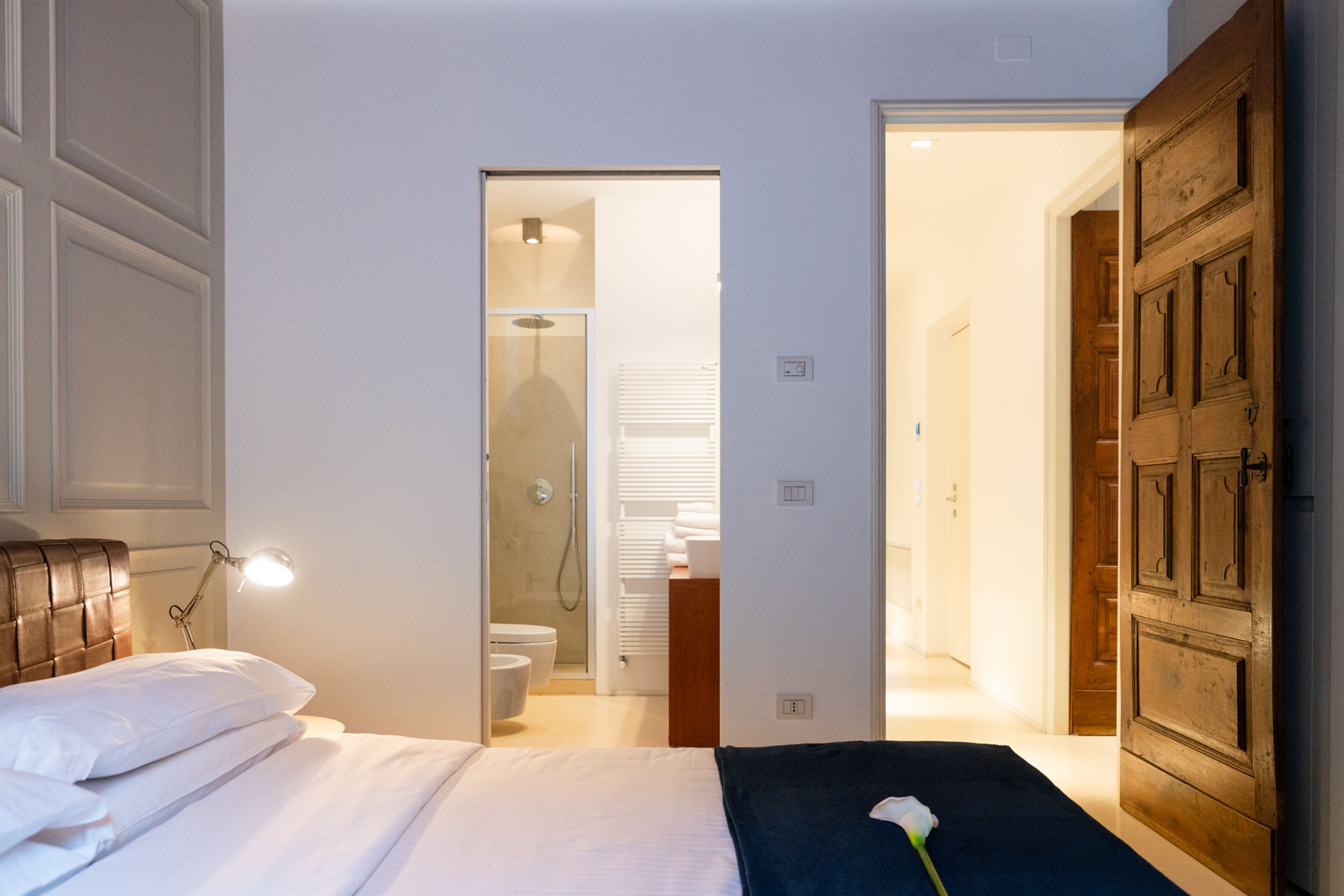 A bedroom with a bed, bedside lamp, and a view into the bathroom.
