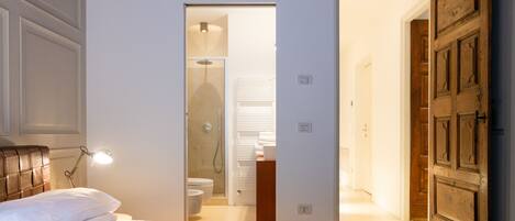 A bedroom with a bed, bedside lamp, and a view into the bathroom.