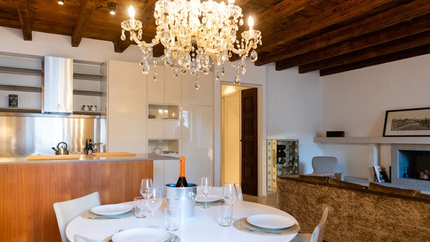 A modern dining area with a round table set for four, a bar area with a bottle of champagne, and a kitchen in the background.