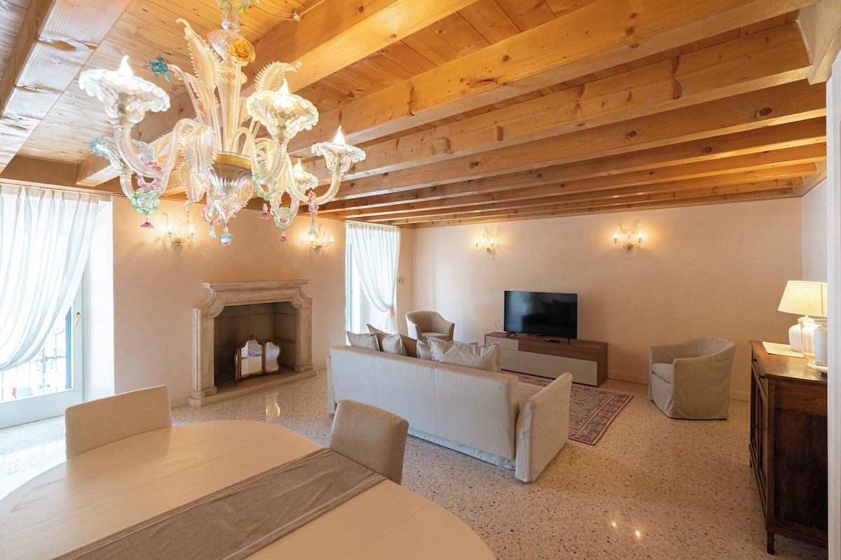 Un salon spacieux avec une cheminée, un canapé, un téléviseur et un lustre.