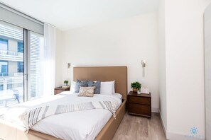 Quarto moderno com uma cama grande, uma mesinha de cabeceira com uma planta e vista para uma varanda.
